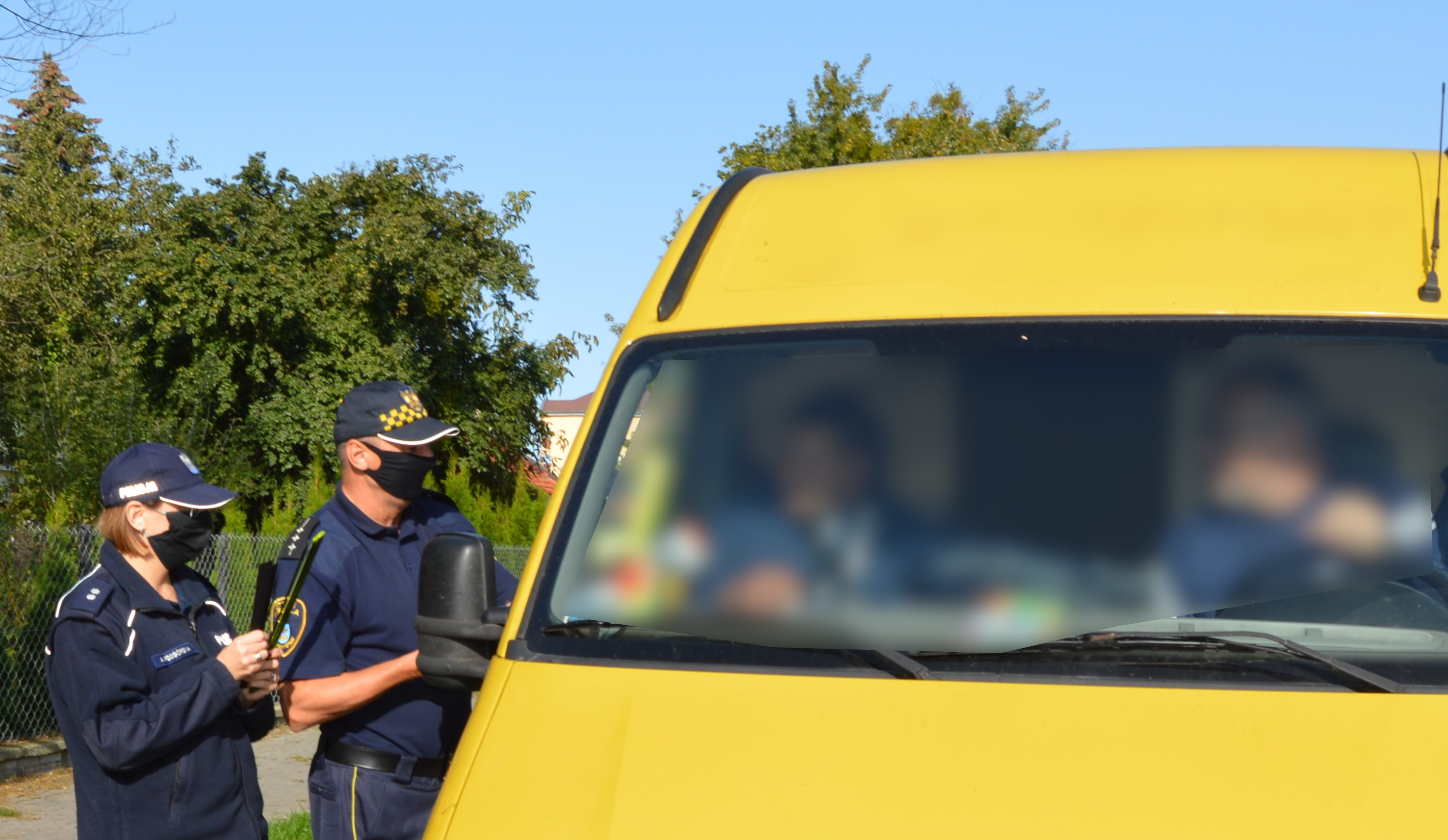policjant i funkcjonariusz Straży Miejskiej rozmawiają z kierowcą i pasażerem samochodu dostawczego